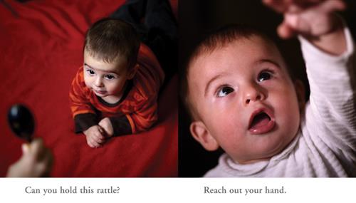  This image is a double page spread. To the left is a photograph of a baby with light skin tone and brown hair. He is lying down on a red blanket. A hand is holding a small black rattle in the foreground. Text: Can you hold this rattle? To the right is a photograph of the baby reaching out to something overhead. Text: Reach out your hand. 
