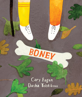  Cover: Boney by Cary Fagan. Illustrated by Dasha Tolstikova. A person’s legs, visible from the knees down, fill the top half of the image. One leg wears a long orange sock, and the other wears a yellow sock with two red stripes at the top. Both feet wear white sneakers. The bottom half of a walking stick is visible. In the center, a white bone lays on the ground among fallen leaves. The bone is long and thick with two rounded sockets on each end. The title is written on the middle of the bone in orange. 