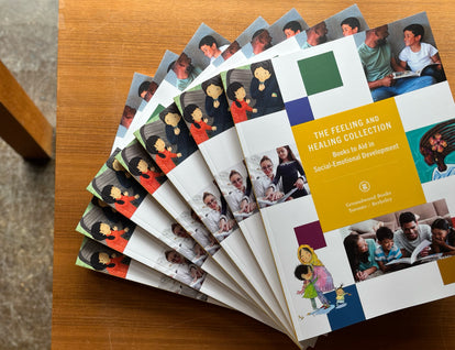 A photograph of seven copies of the Feeling and Healing Catalogue fanned out on a wooden table. 