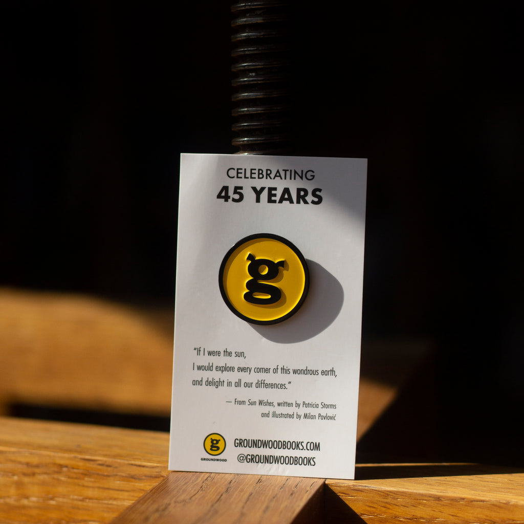  Photo: A circular enamel pin emblazoned with the Groundwood Books logo. The pin is attached to a white rectangular card which reads 