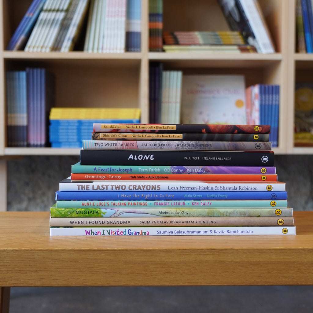  Photo of books featured in the Exploring Culture and Identity bundle. The books are stacked on a wooden stool, with bookshelves in the background. The spines face out. 