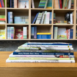  Photo of the books in the Fostering Inclusion and Acceptance Bundle stacked on a wooden stool, with bookshelves in the background. The spines face out. 