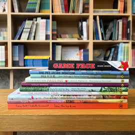  Photo of books featured in the Navigating Specific Emotions bundle. The books are stacked on a wooden stool, with bookshelves in the background. The spines face out. 