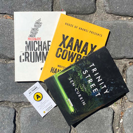  Photo: The poetry anthologies Passengers, Xanax Cowboy, and Trinity Street lay fanned out against a background of cobblestones. Below them sits a decorative House of Anansi Press Logo enamel pin. 
