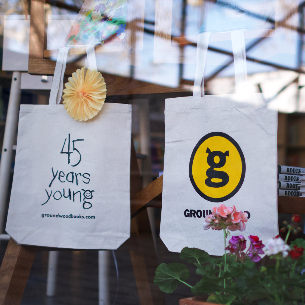  Photo: In a shop window hang two white tote bags. One is rotated to show the side printed with 