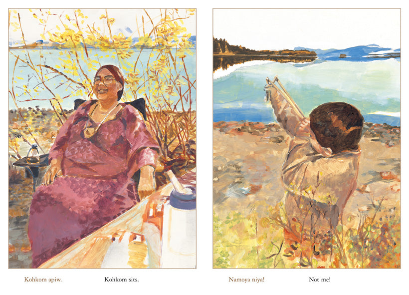  This image is a double page spread. To the left is the shore beside a lake. The ground is full of leaves and sparse bushes. A woman with medium skin tone sits by a table. She smiles. Text: Kohkom sits. To the right is the lake and a rocky shore. A boy holds a slingshot up to his face, which he aims out toward the water. Text: Not me! 
