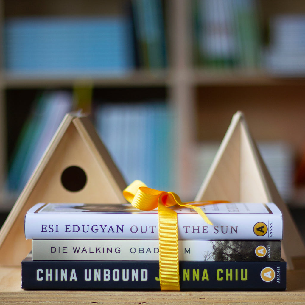 A photo of copies of Out of the Sun, Die Walking, and China Unbound in a stack on a wooden surface, tied  together with a bright yellow ribbon. Two unvarnished pine bird houses sit behind them in the background. 