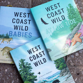  A photo of copies of West Coast Wild Babies, West Coast Wild at Low Tide, and West Coast Wild, all hardcover picture books, laying on a cement surface. 